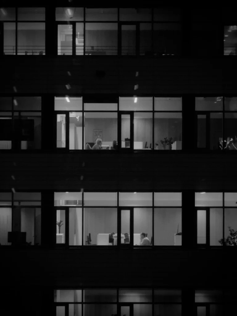 Office towers lit from within after dark, seen from across the street